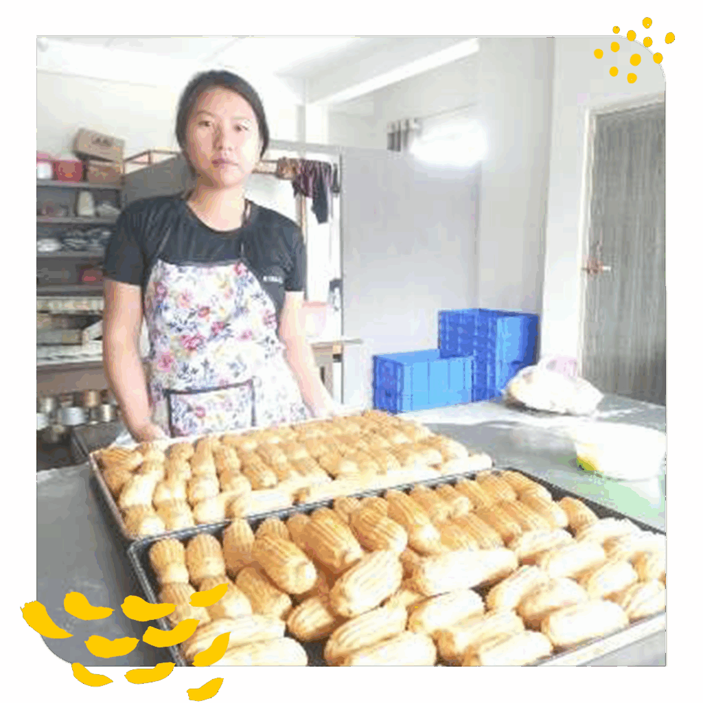 A young woman stands behind two trays of freshly baked rolls